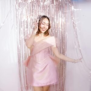 Young woman smiling in a pink dress amidst glistening tinsel, exuding elegance and glamour.