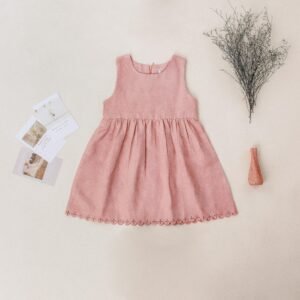 Pink child's dress laid on beige background with decorative vase and postcards, styled in a modern flat lay.