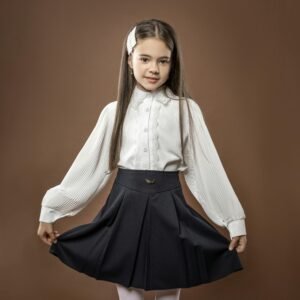 Young girl in a studio wearing a white blouse and black skirt against brown background.